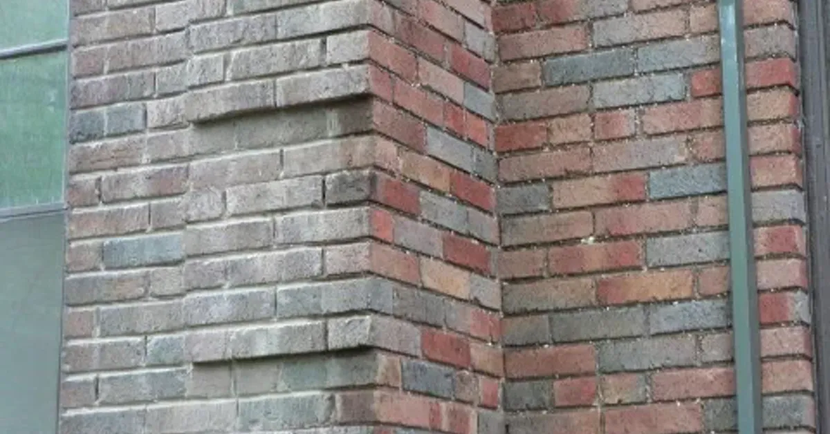 A brick wall corner mid-tuckpointing: right side restored with fresh, color-matched mortar joints, left side ground out and ready for repointing