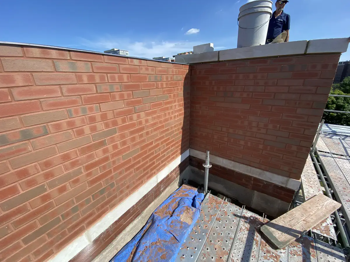 Chicago brick parapet wall mid-rebuild with crew member on scaffolding during grinding work